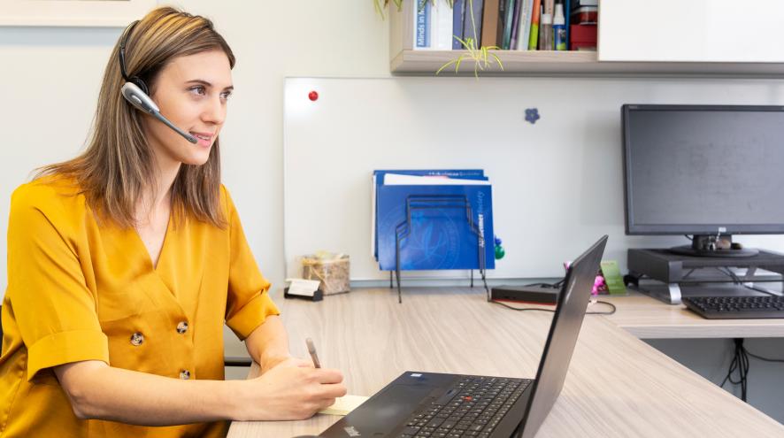 Helpline volunteer dressed in yellow at the laptop and listening intently.