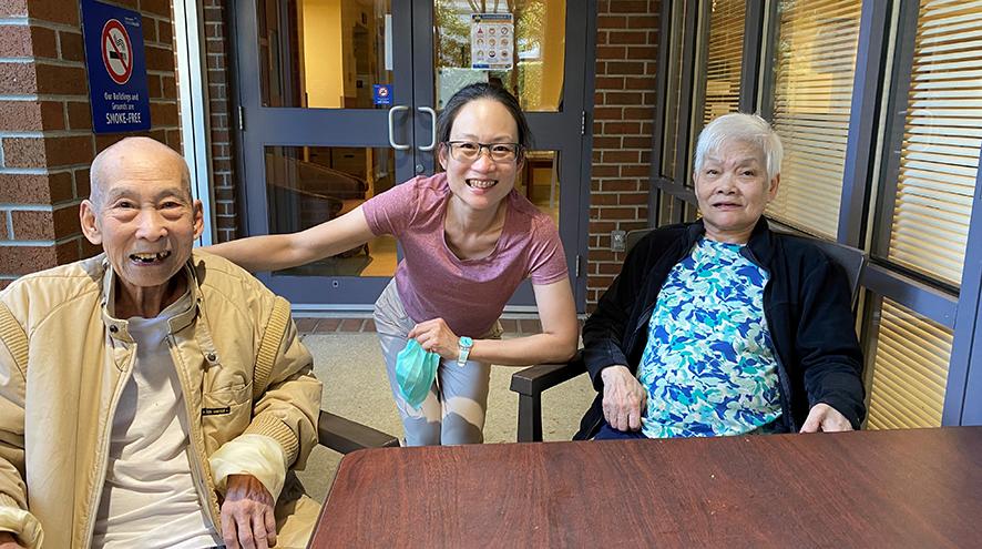 A younger woman hovers across a table, with an older man, her father on one side and her older mother on the other side.