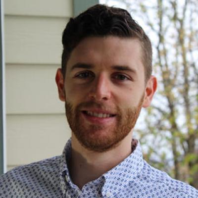 Nathan smiling in front of a house and trees.