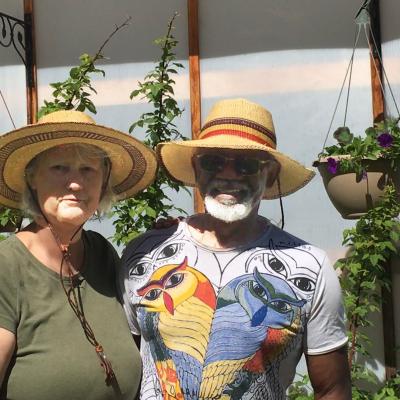 Birgit and Granville wearing straw hats on a sunny day in front of a colourful background.