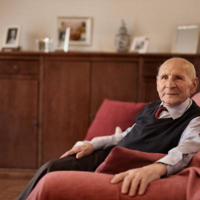 Elderly man sitting in a sofa, looking up at the camera.