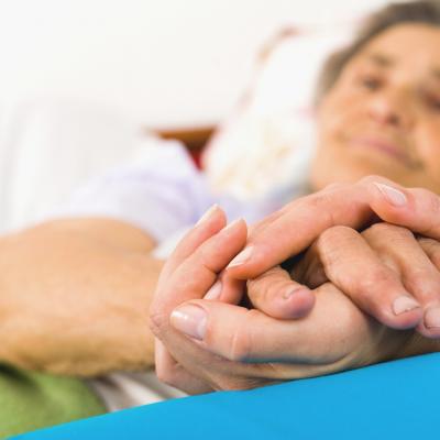 An elderly woman smiling and holding another person's hand.