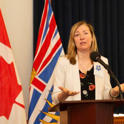 Maria speaking in front of the Canadian and British Columbian flag.