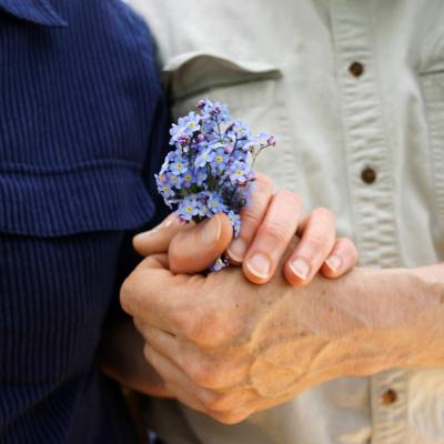 Two people holding hands, with a bundle of forget-me-not flowers.