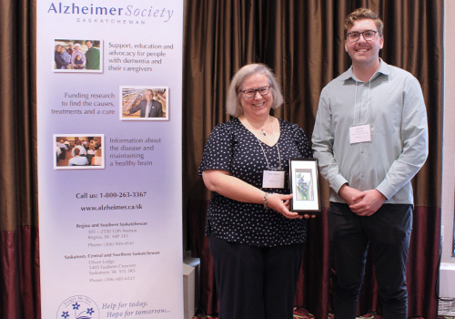 Dr. Debbie Maurer is standing in front of an Alzheimer Society banner while holding her Philanthropic Leadership Award